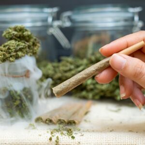 Woman hand holding Pre-Rolled cones for smoking cannabis with cannabis indica in a clear bottle