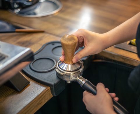 Close-up of hand Barista cafe making coffee. Preparing for an espresso shot. High quality photo. Barista making coffee with manual presses ground coffee using tamper at the coffee shop.